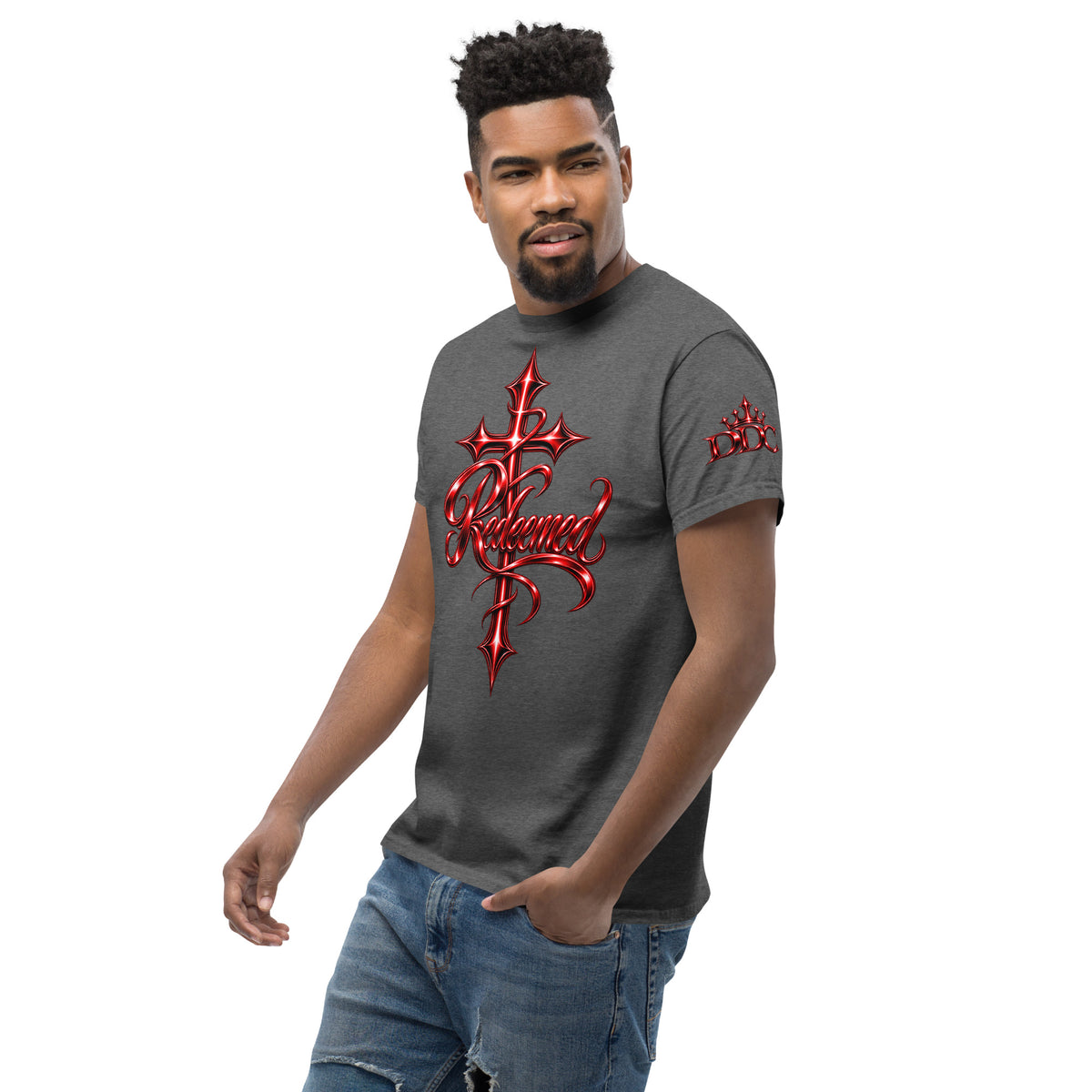 A man wearing a dark gray t-shirt with a red gothic cross and the word 'Redeemed' printed on the front, paired with blue jeans, set against a plain white background