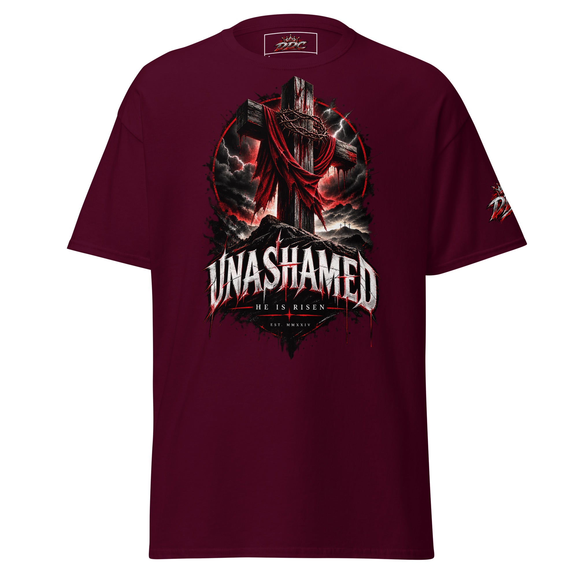 A maroon short-sleeve t-shirt with a large graphic print on the front featuring a cross, a draped figure, and the text 'UNASHAMED' and 'HE IS RISEN'.
