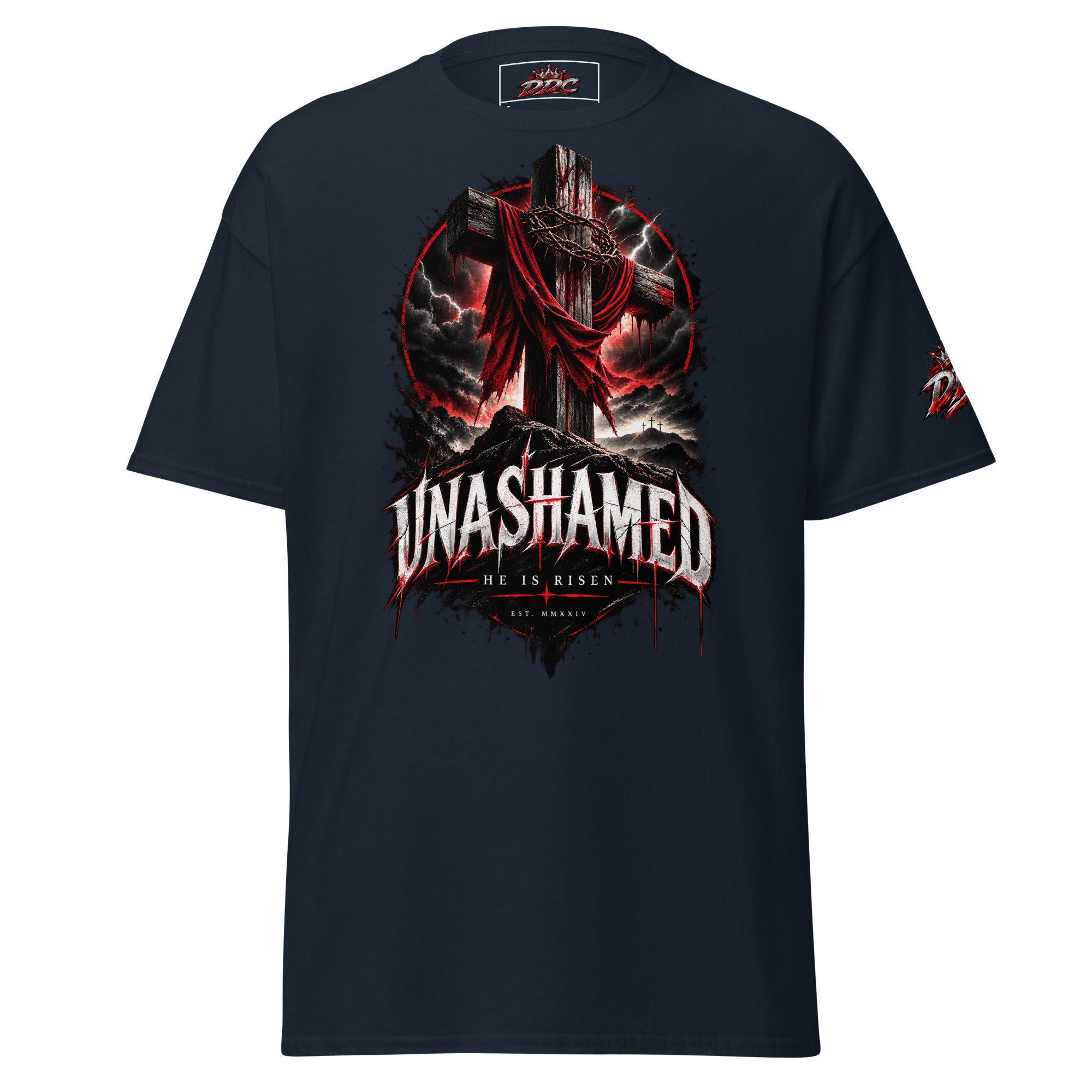 A navy blue short-sleeve t-shirt with a large graphic print on the front featuring a dark cross draped in red cloth, stormy clouds, and the text 'UNASHAMED' and 'HE IS RISEN'. A smaller matching graphic is visible on the right sleeve.