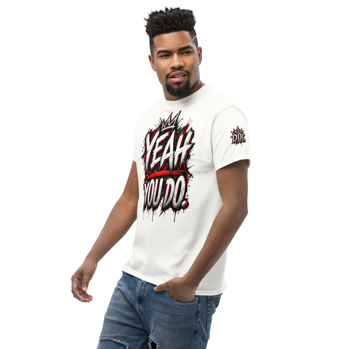 A man wearing a white graphic t-shirt with a red and black 'Yeah You Do' design on the front, paired with blue jeans, set against a plain white background.