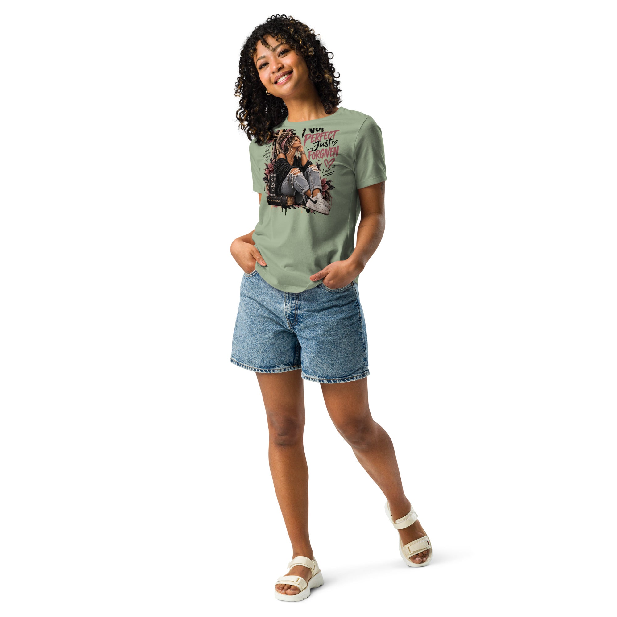 A woman modeling a sage green graphic t-shirt with denim shorts and white sandals, standing against a solid white background.