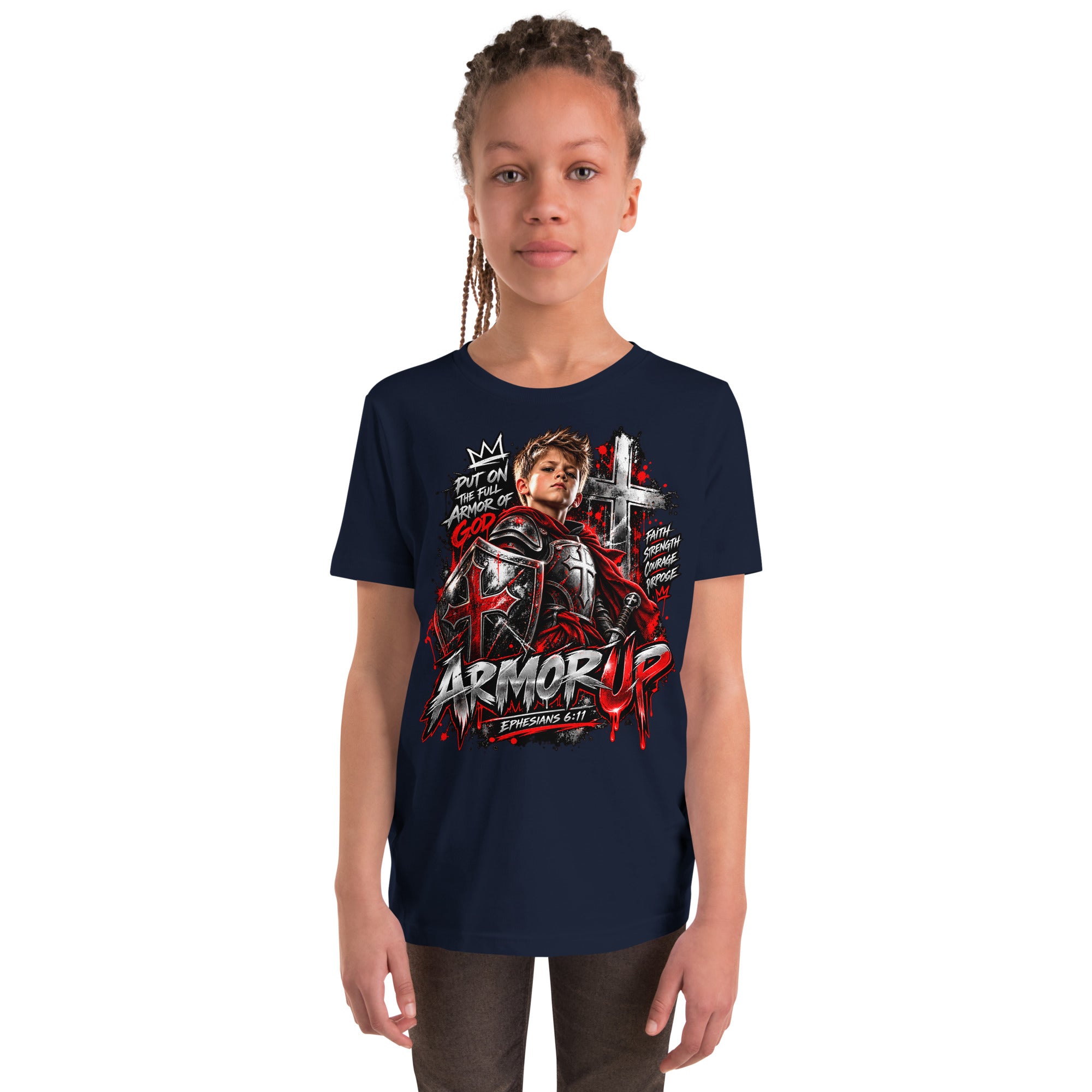 A young girl with braided hair stands against a plain white background wearing a navy blue graphic t-shirt. The shirt features a large front print with a knight in armor, a cross, and the text 'ARMOR UP' and 'ST.